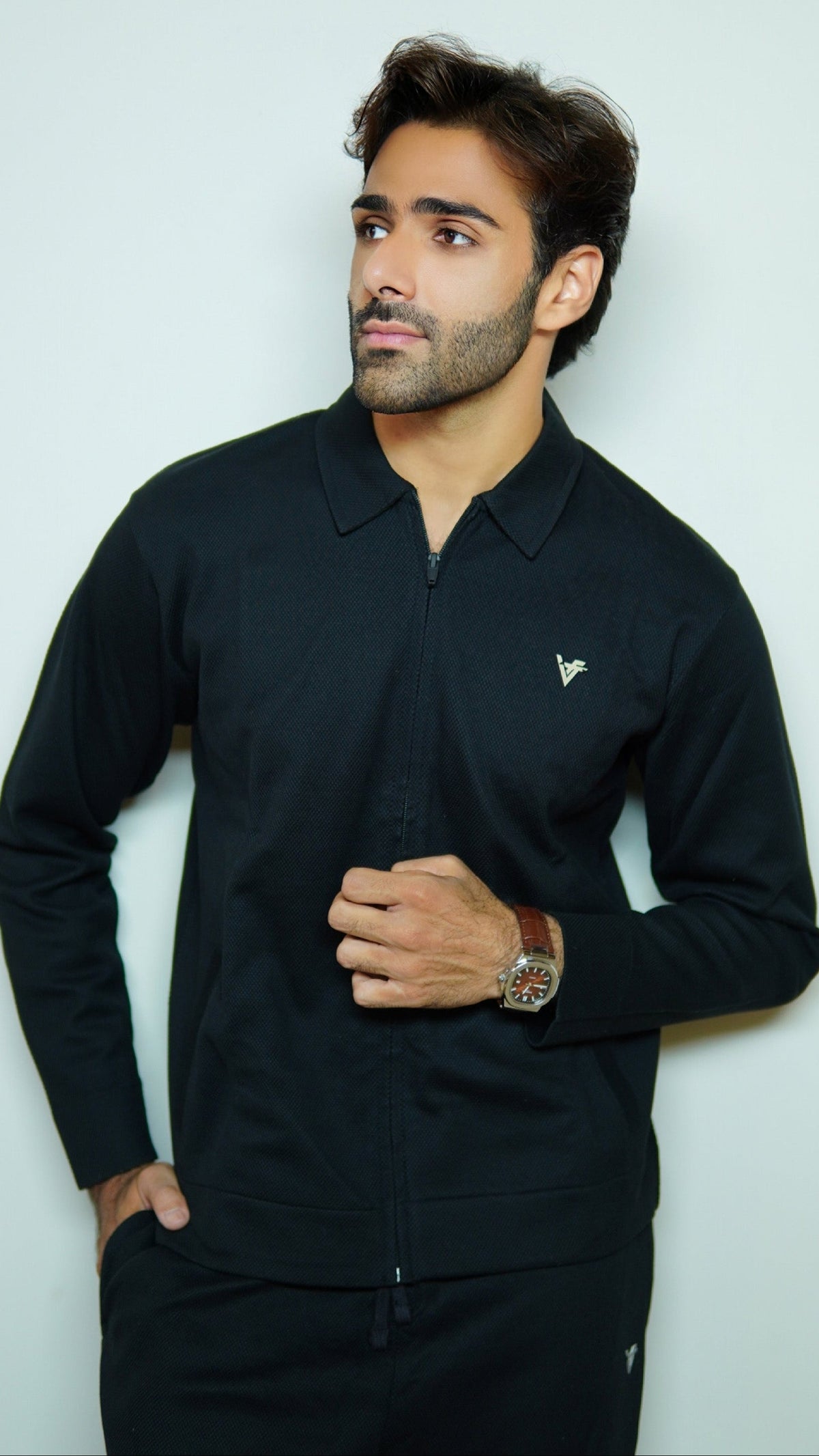 Man wearing a black long-sleeve shirt with a small logo on a light gray background