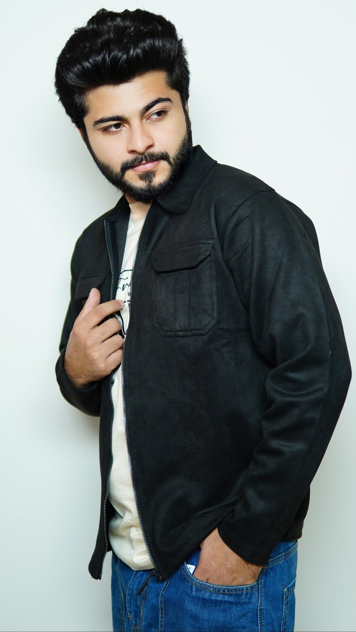 Man wearing a black jacket over a white shirt with a plain background
