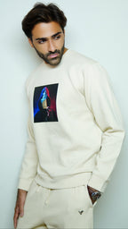 Man wearing a cream sweatshirt with a colorful graphic design on a light gray background