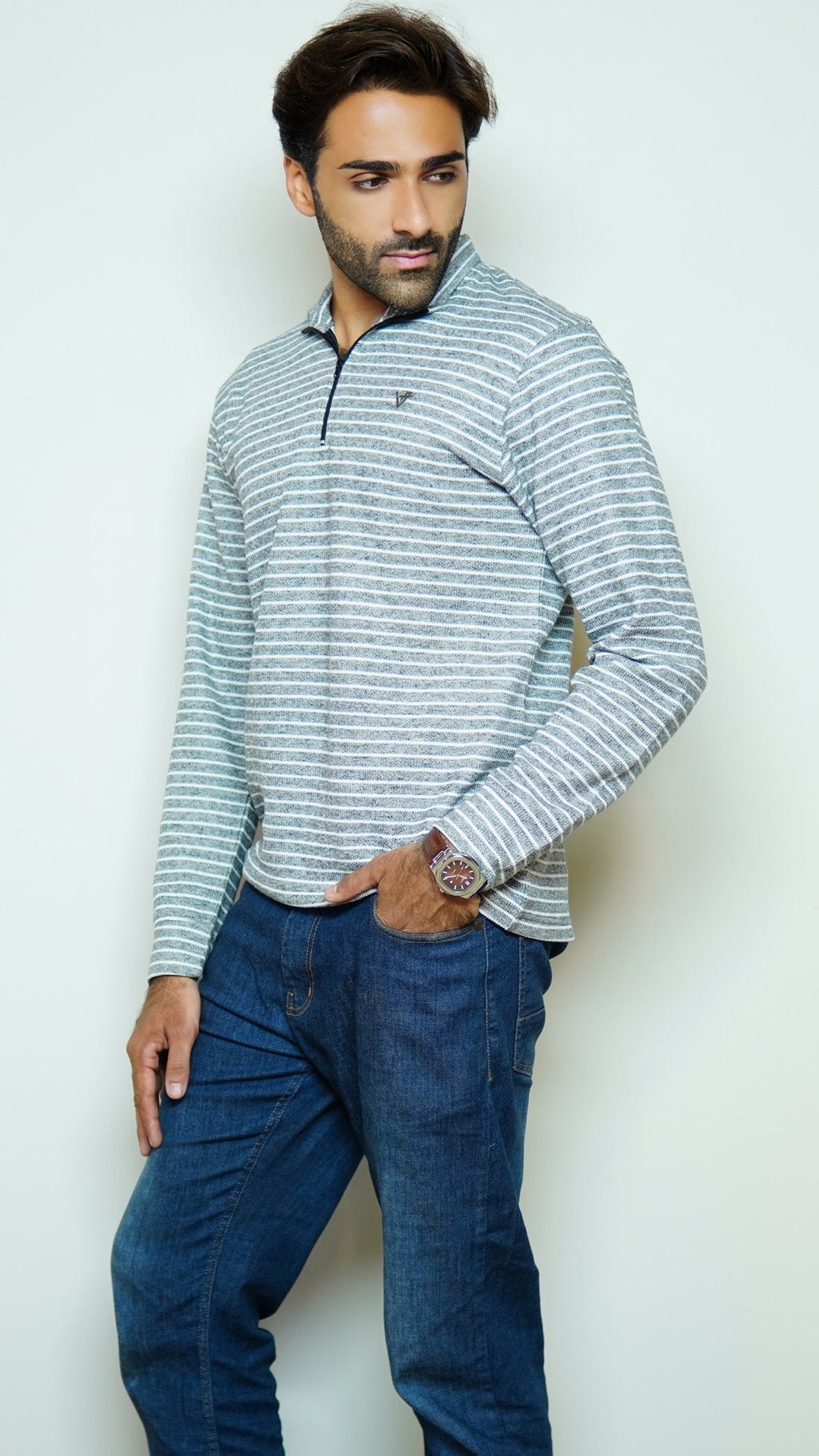 Man wearing a striped sweater and blue jeans against a plain background