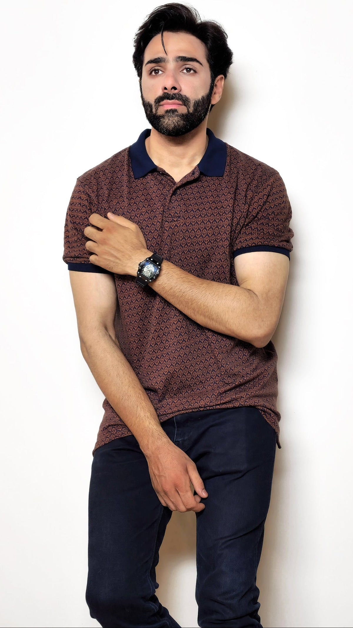 Man wearing a patterned polo shirt and jeans on a white background